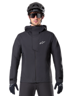 Alpinestars A-Dura Elite vattentät jacka, svart MTB-jacka, design med hög krage och huva, dragkedja fram med skyddande bröstflik och vit logotyp, bärs med svart hjälm och cykelhandskar, tekniskt väderskydd för trailcykling