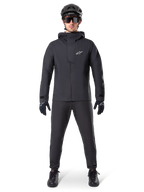 Alpinestars A-Dura Elite vattentät jacka, svart, bärs med matchande cykelbyxor och handskar, svart hjälm och solglasögon, med en vit Astars-logotyp på bröstet, högpresterande teknisk design för mountainbike