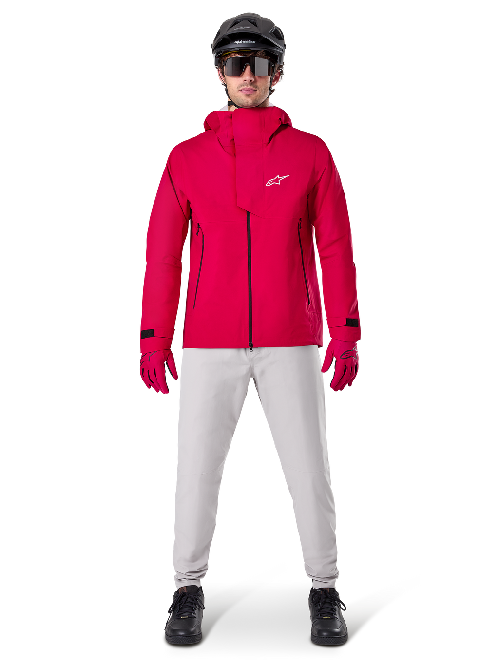 Alpinestars A-Dura Elite vattentät jacka, röd fluo, teknisk mountainbikejacka som bärs med en svart MTB-hjälm, solglasögon, matchande röda handskar och ljusgrå byxor, helkroppsvy av cykelutrustning för alla väder