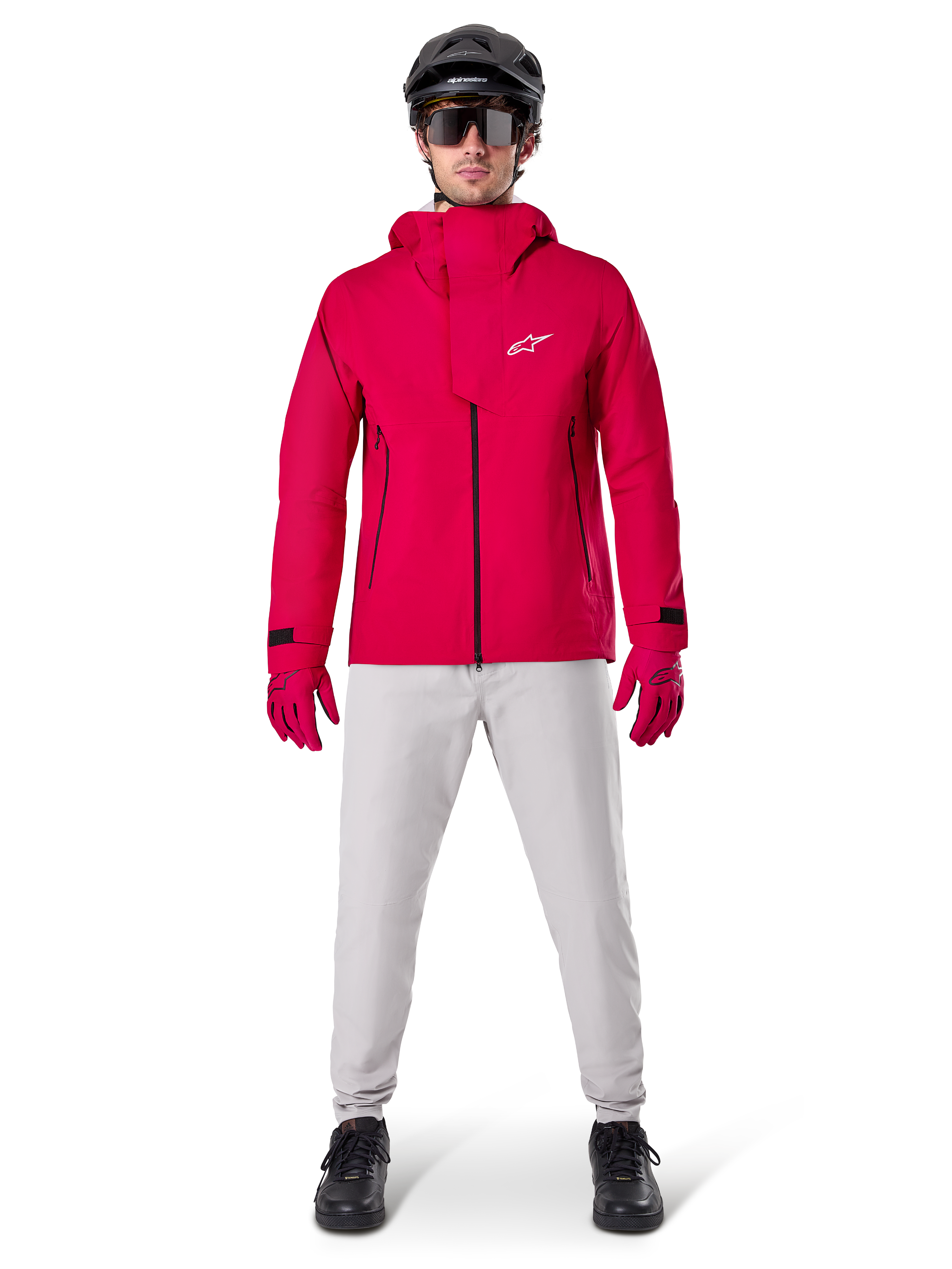 Alpinestars A-Dura Elite vattentät jacka, röd fluo, teknisk mountainbikejacka som bärs med en svart MTB-hjälm, solglasögon, matchande röda handskar och ljusgrå byxor, helkroppsvy av cykelutrustning för alla väder