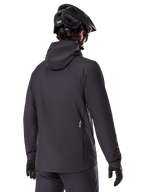 Alpinestars A-Dura Thermal Jacket, svart, vy bakifrån, bärs med en svart mountainbikehjälm och handskar, har en liten vit Astars-logotyp på nedre delen av ryggen, lätt isolerad cykeljacka
