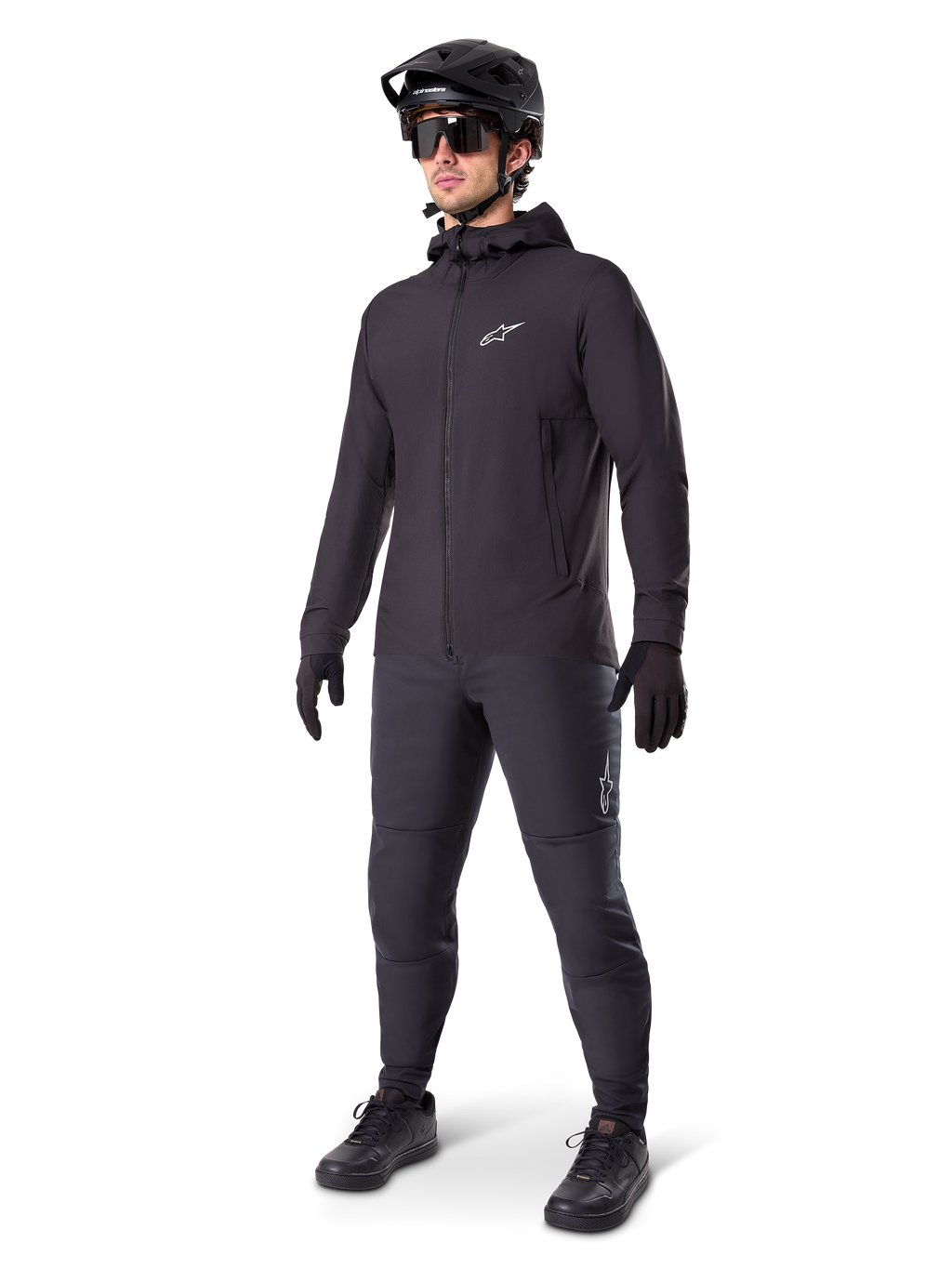 Alpinestars A-Dura Thermal Jacket i svart, bärs av en manlig cyklist med komplett mountainbike-utrustning inklusive svart hjälm, solglasögon och cykelbyxor, lätt isolerad jacka med huva för prestation i kallt väder.