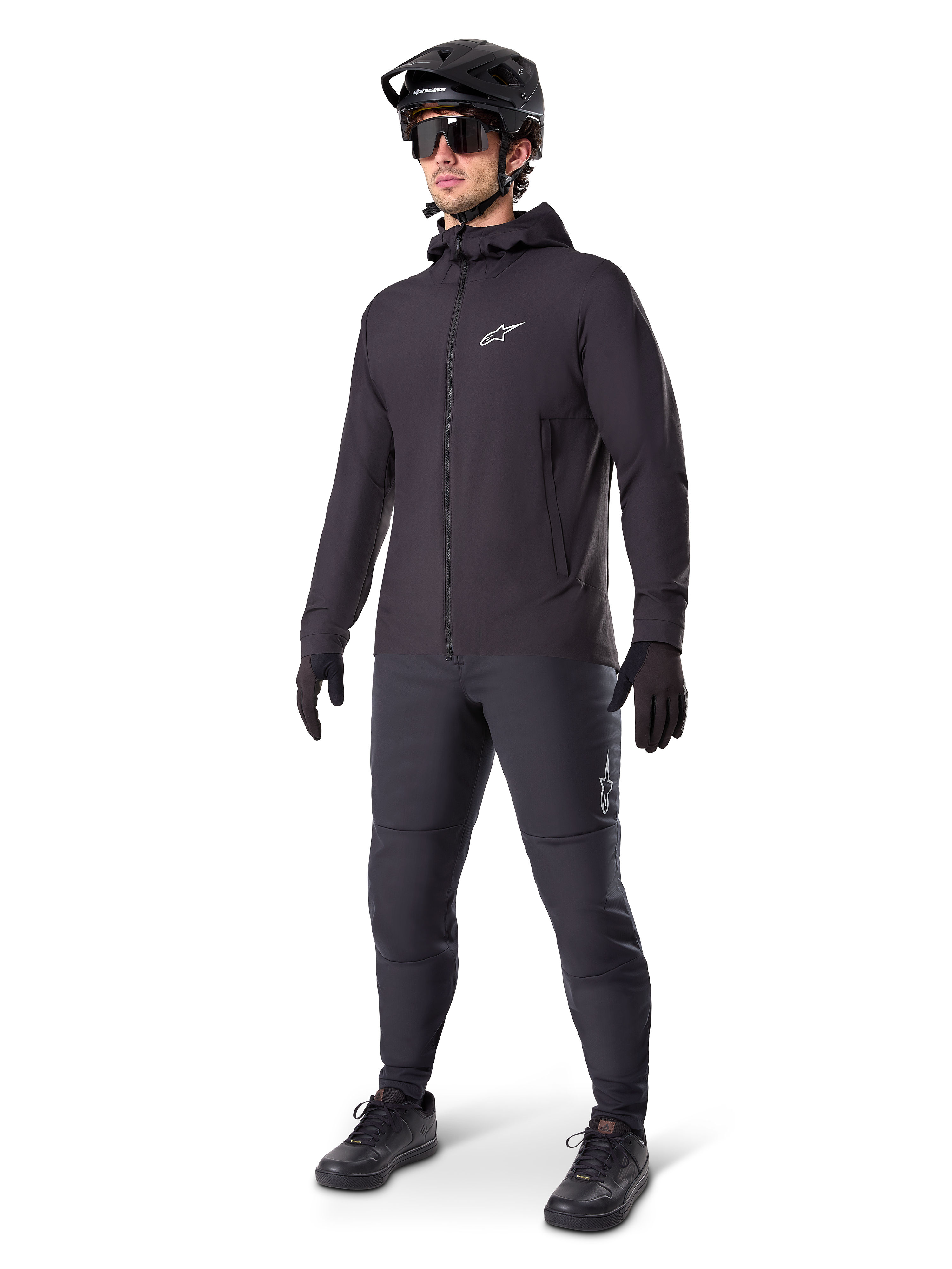 Alpinestars A-Dura Thermal Jacket i svart, bärs av en manlig cyklist med komplett mountainbike-utrustning inklusive svart hjälm, solglasögon och cykelbyxor, lätt isolerad jacka med huva för prestation i kallt väder.