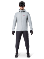 Alpinestars A-Dura Thermal Jacka, titaniumgrå, cykeljacka bärs med svarta mountainbikebyxor, handskar och hjälm, med en liten röd stjärnlogotyp på bröstet och hel dragkedja fram, lätt isolerad utrustning för terrängkörning
