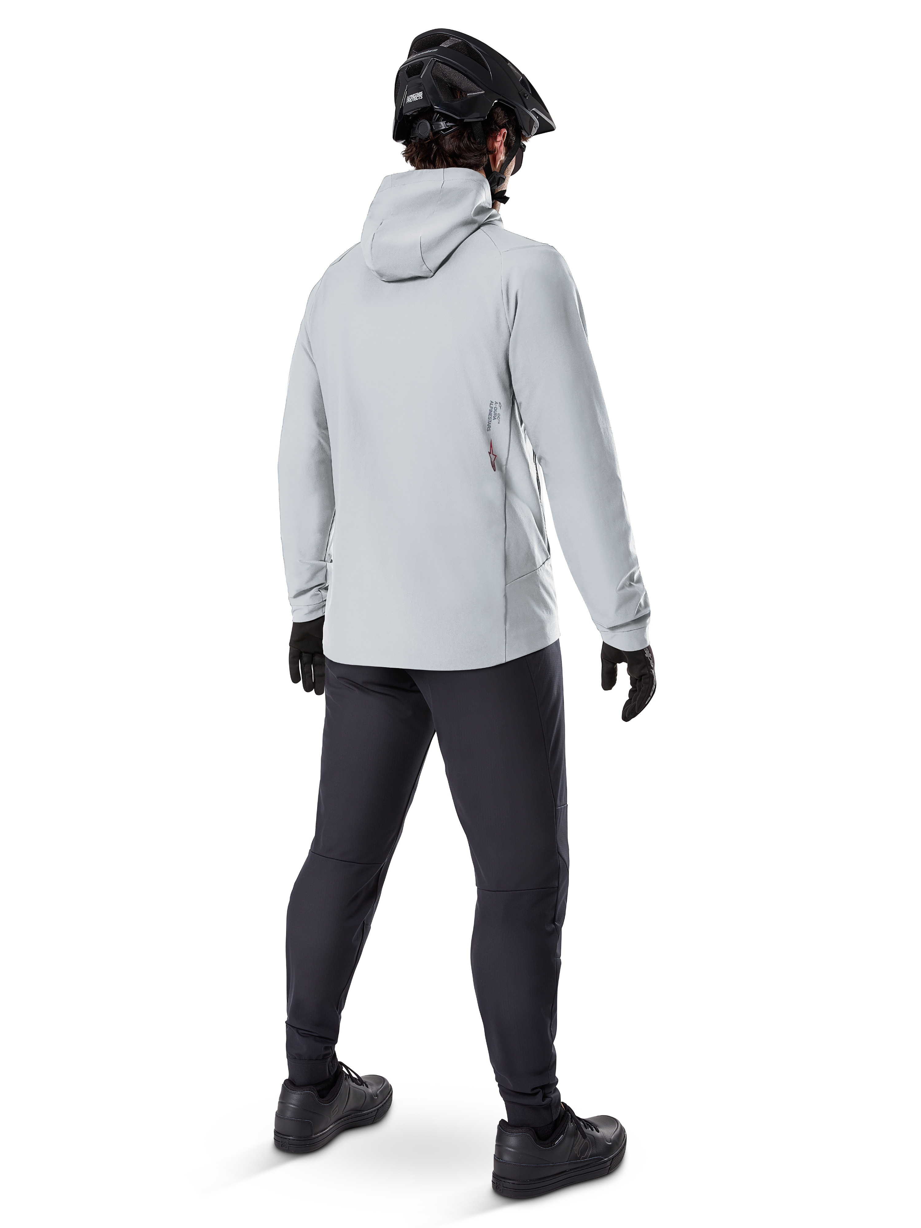 Alpinestars A-Dura Thermal Jacket i Titanium, vy bakifrån av en manlig cyklist i en ljusgrå termojacka med huva, matchad med svart MTB-hjälm, svarta handskar och mörkgrå byxor, funktionell utrustning för mountainbikecykling.