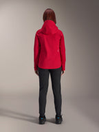 Ryggvy av en kvinna som bär Alpinestars Stella A-Dura Elite Waterproof Jacket i Red Fluo, stylad med svarta byxor och skor, med en skyddande huva och längre bakfåll för mountainbike.