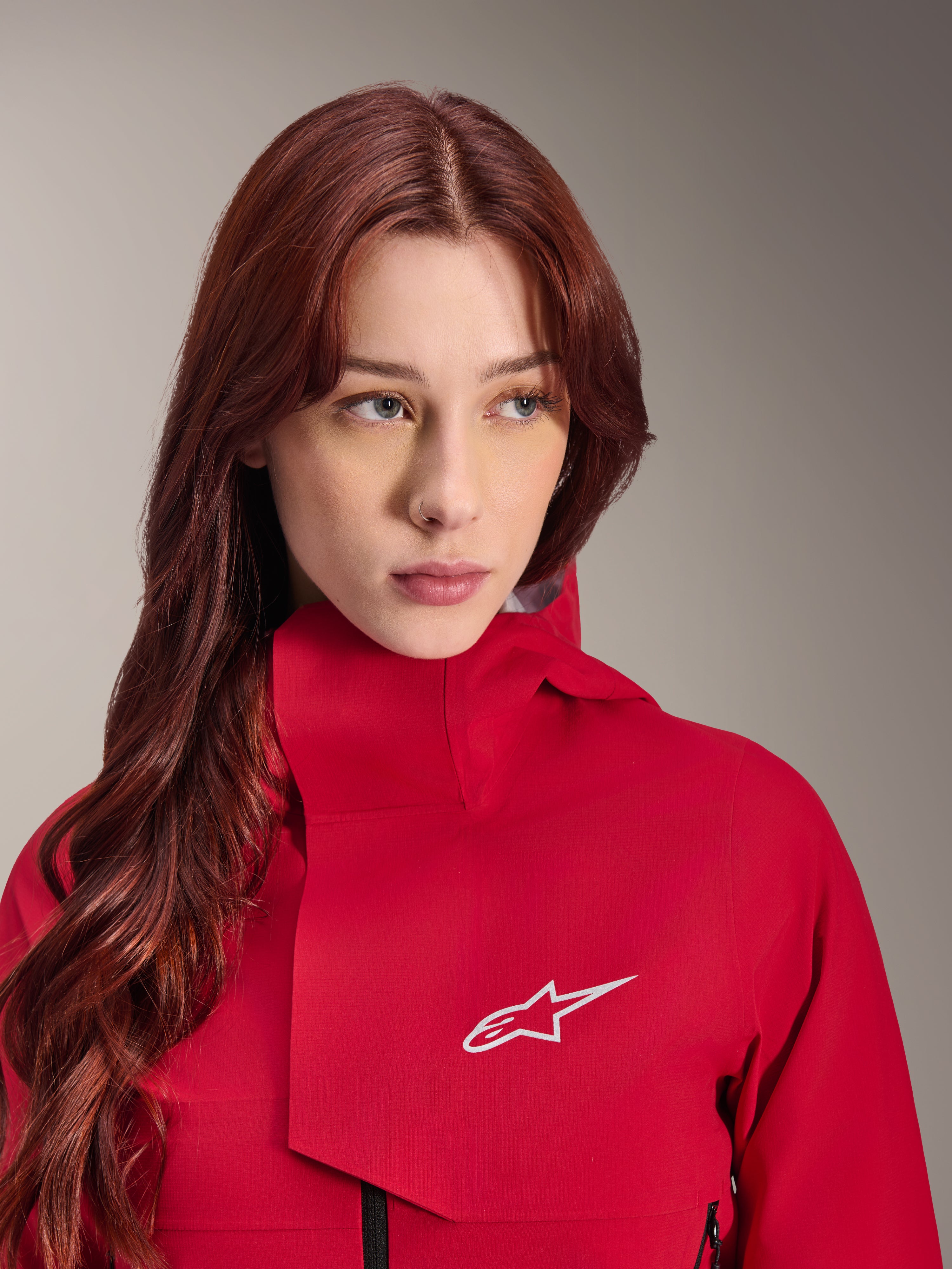 Alpinestars Stella A-Dura Elite vattentät jacka, Red Fluo, bärs av en kvinna med långt rött hår, teknisk 3-lagers vattentät jacka med hög krage och vit logotyp, högpresterande outdoor- och mountainbikeutrustning