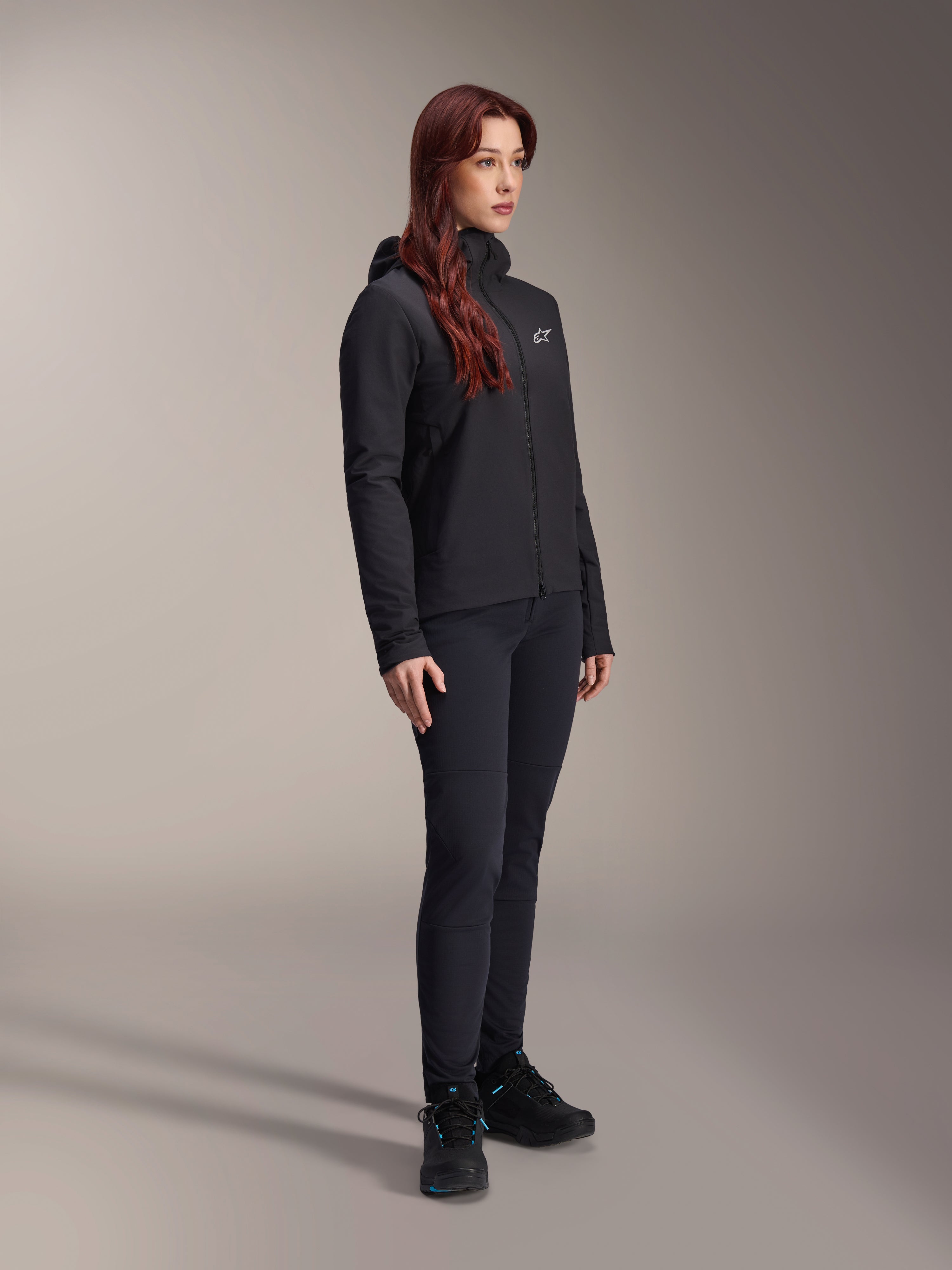 Alpinestars Stella A-Dura Thermal Jacket, svart lättviktig isolerad damjacka med huva, bärs med svarta byxor och svarta skor, professionell outfit för cykling och mountainbike under kalla förhållanden