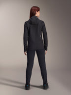 Kvinna som bär Alpinestars Stella A-Dura Thermal Jacket, sedd bakifrån, svart isolerad cykeljacka med huva, matchande svarta byxor och skor, med en liten vit logotyp på nedre delen av ryggen