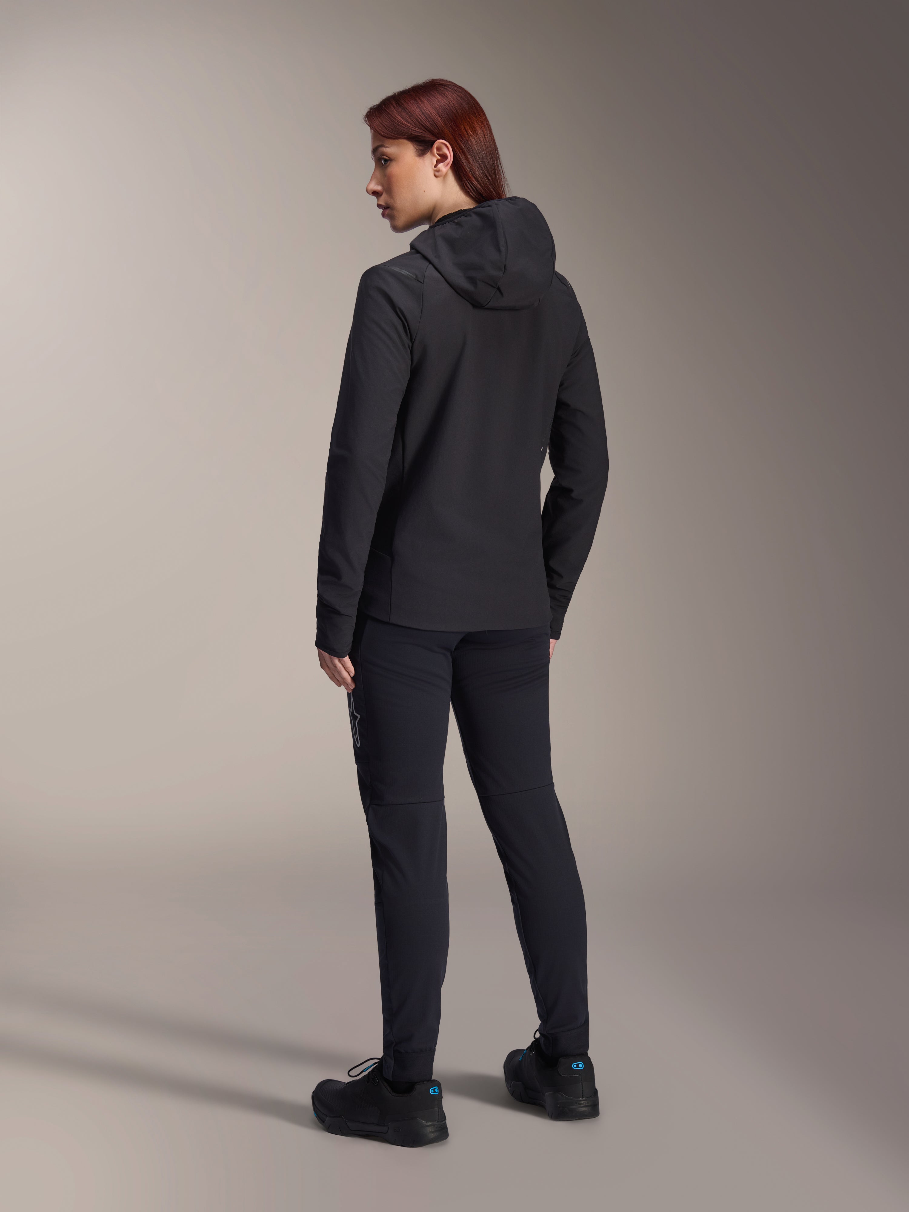 Alpinestars Stella A-Dura termojacka, MTB-cykeljacka för dam, svart, vy bakifrån som framhäver den isolerade huvan och normal passform, bärs med matchande svarta byxor och skor, lätt termisk isolering för cykling i kallt väder