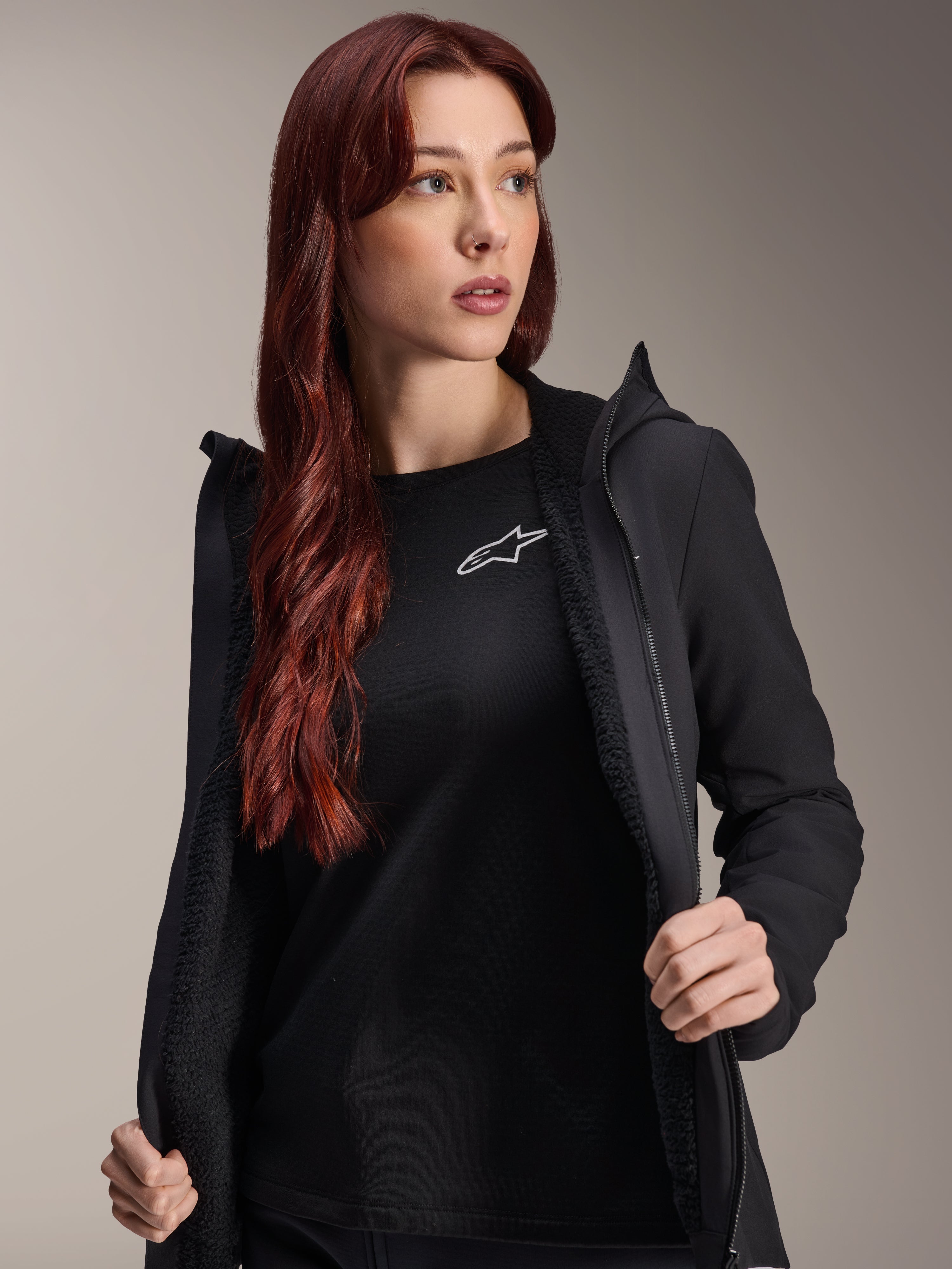 Alpinestars Stella A-Dura Termojacka, svart cykeljacka för damer, visas öppen med strukturerat fleecefoder och dragkedja framtill, buren över en svart t-shirt med Alpinestars-logotypen, lätt och isolerad för cykling i kallt väder