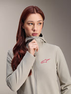 Alpinestars Stella A-Dura Thermal Jacket för dam, titaniumgrå med en rosa Alpinestars-stjärnlogotyp, modell med långt rött hår som bär och drar upp dragkedjan på den huvförsedda jackan, lätt isolerad cykelbeklädnad för kallt väder.