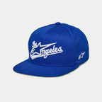 Alpinestars Los Angeles Hat, blå snapback-keps med platt skärm, vitt 3D-broderat 'Los Angeles' i atletiskt typsnitt, Ageless-logotyp på sidan, strukturerad krona, vardaglig motorsport-inspirerad huvudbonad