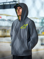 Alpinestars Speeder Chromium Windbreak Jacket, koksgrå livsstilsjacka med neongula detaljer, design med huva, gult innerfoder och logotyp på bröstet, avslappnad motorsport-streetwear som bärs av en modell i utomhusmiljö