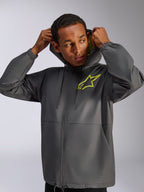 Alpinestars Speeder Chromium vindjacka, koksgrå och neongul, manlig modell som bär vindjacka med huva och dragsko, neongul Alpinestars-logotyp på bröstet och gult foder i huvan, vardaglig motorsportinspirerad streetwear