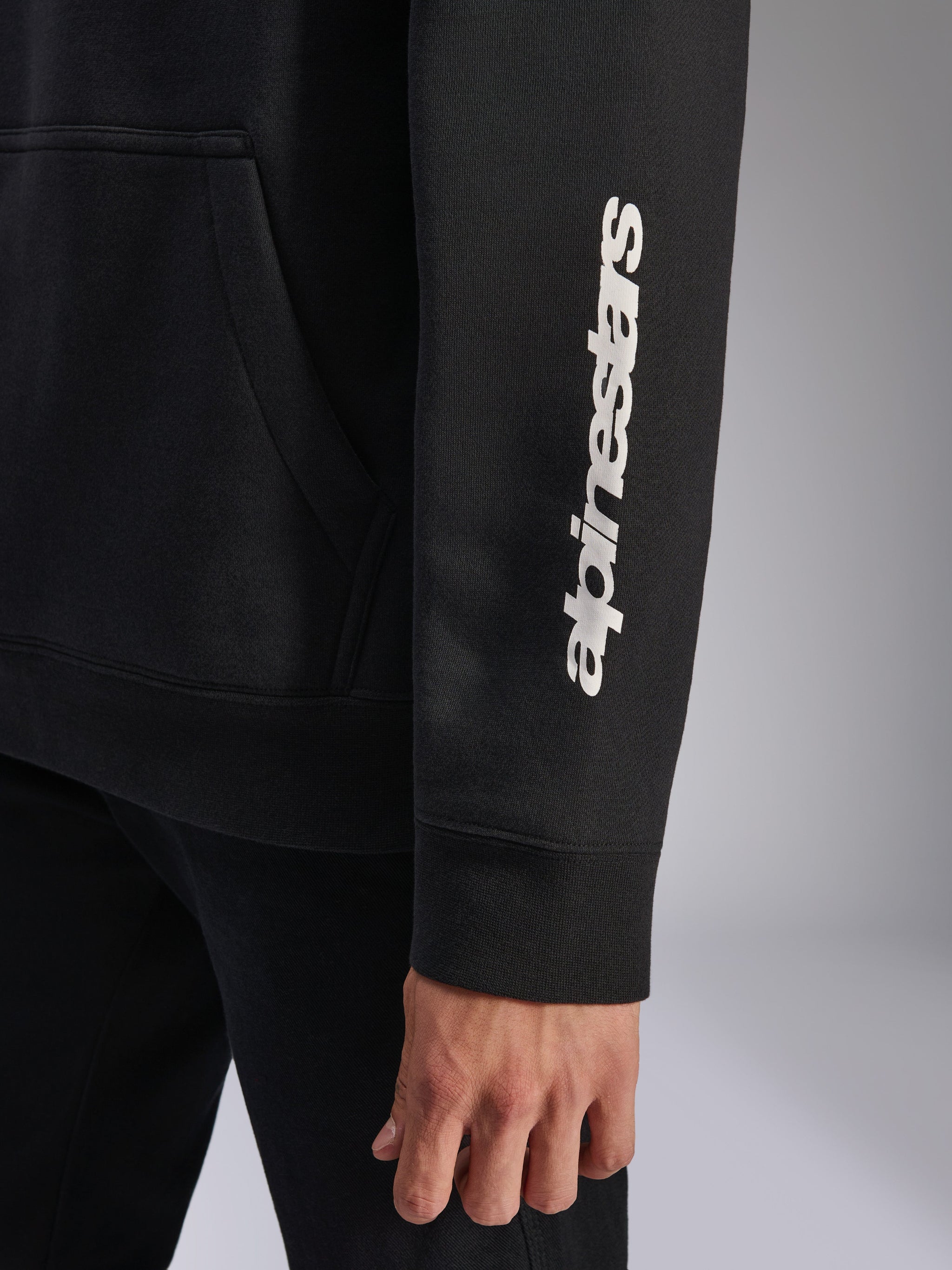 Alpinestars Harken Hoodie, Black, close-up of sleeve featuring vertical white wordmark logo, ribbed cuff and kangaroo pocket detail, casual sportswear fleece