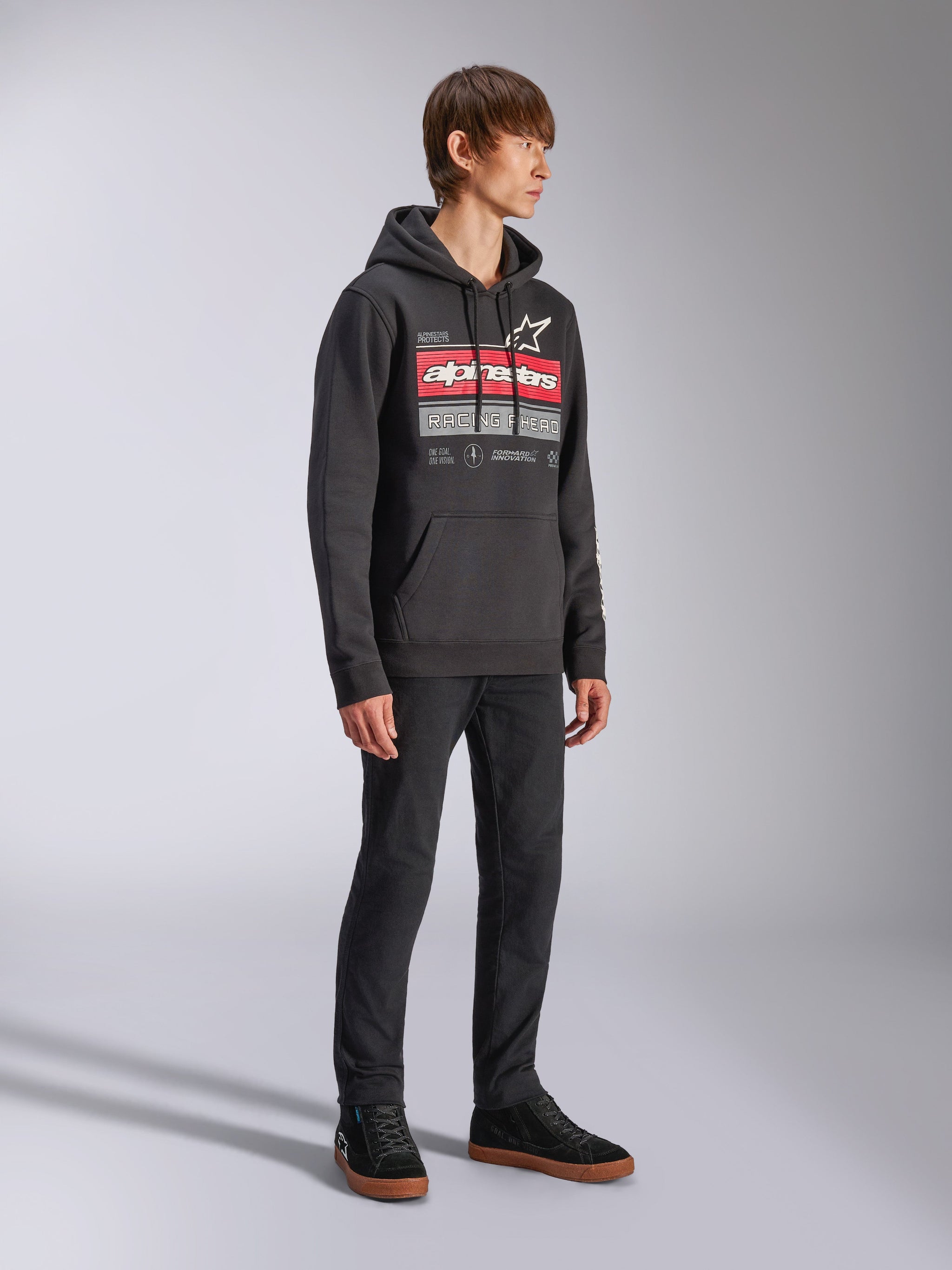 Alpinestars Harken Hoodie, Black pullover fleece hoodie, featuring a large chest graphic with red Alpinestars wordmark and star logo, kangaroo pocket, worn by a model with black pants and sneakers, casual motorsport streetwear
