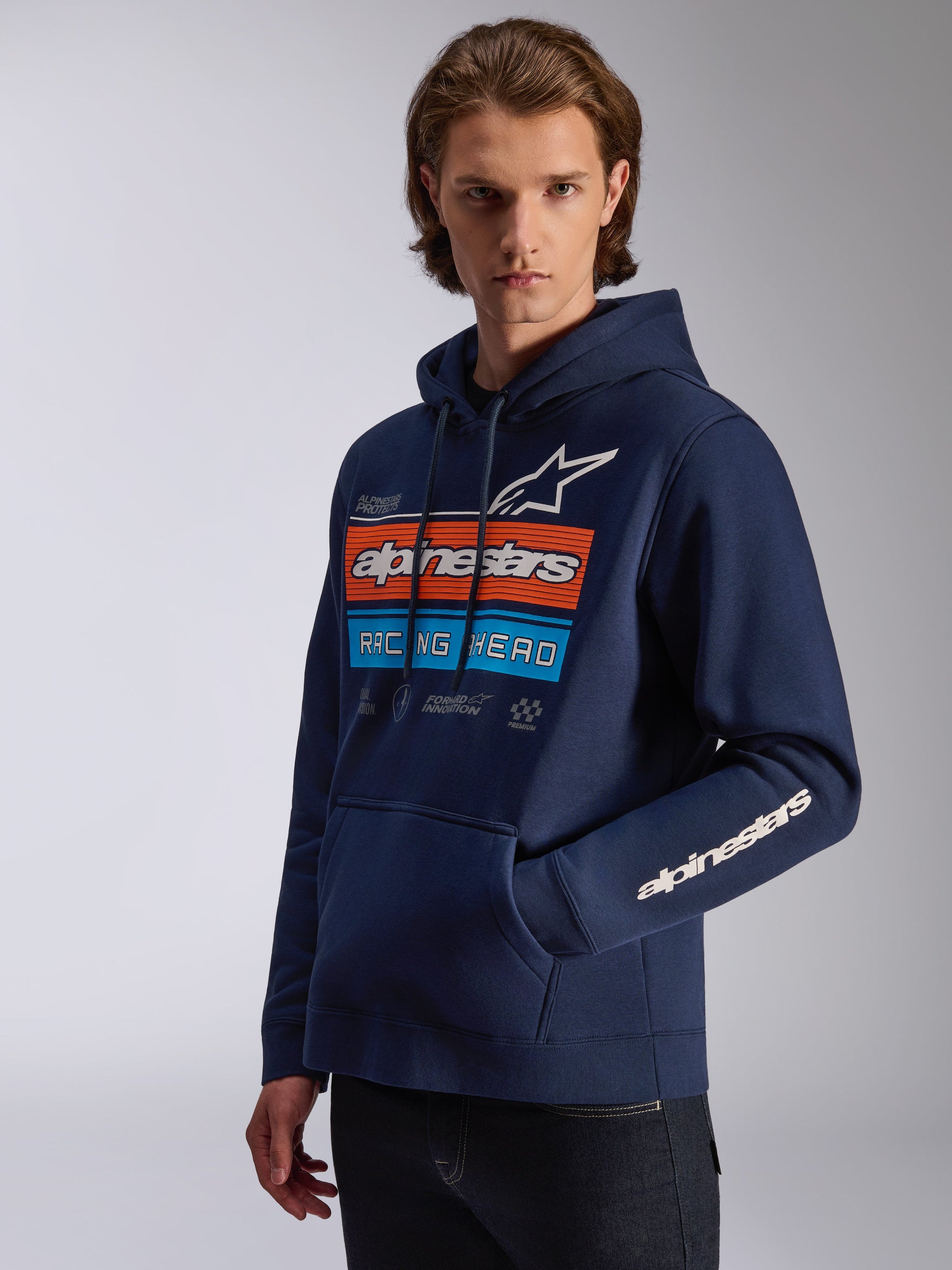 Alpinestars Harken Hoodie, Navy Blue, worn by model, featuring a bold chest graphic with orange and blue 'Racing Ahead' design, Alpinestars wordmark on the sleeve, kangaroo pocket, and drawstring hood