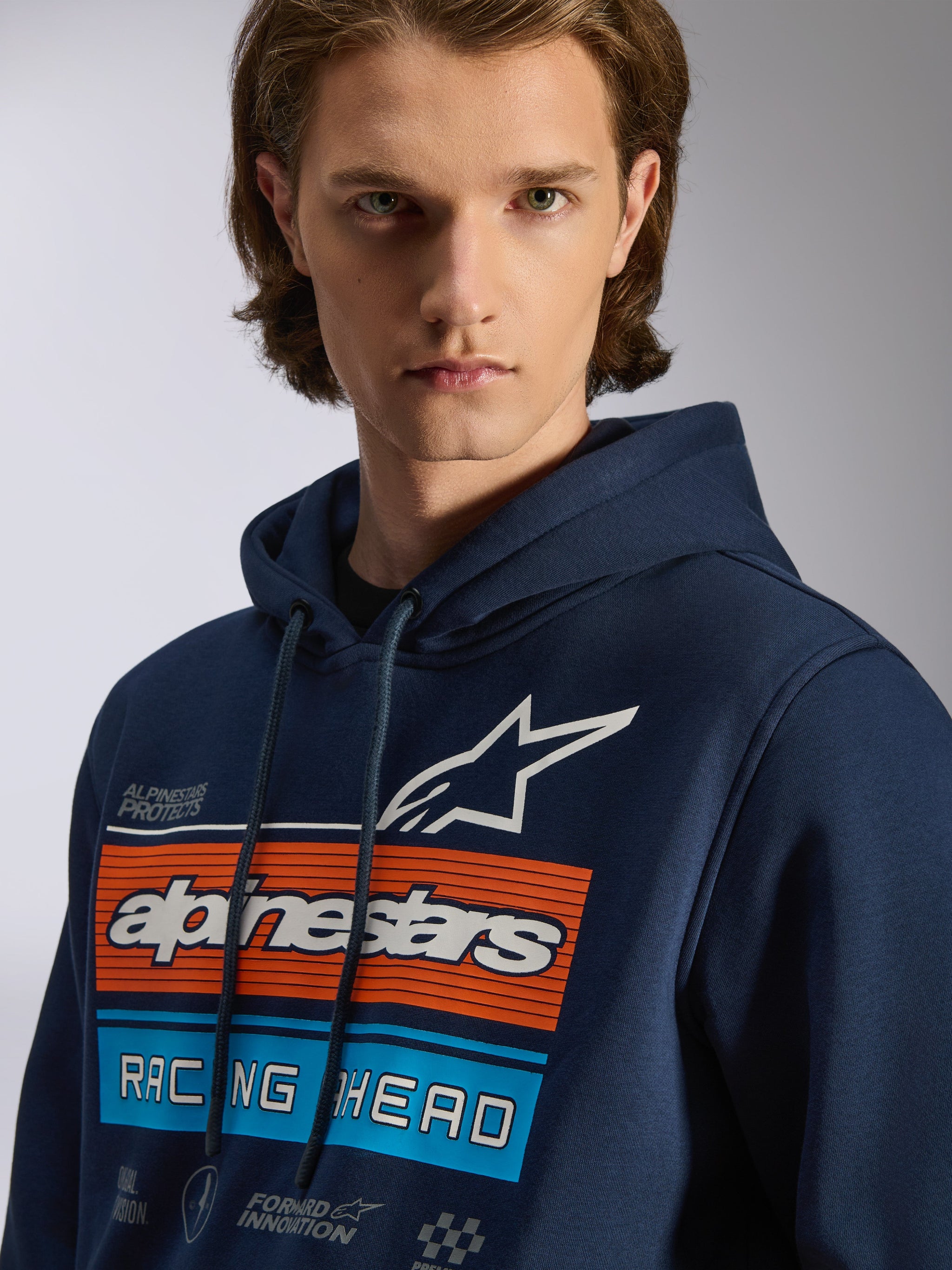 Alpinestars Harken Hoodie, Navy Blue pullover hoodie, chest graphic with orange and light blue horizontal bars, white star logo, 'Racing Ahead' text, casual motorsport streetwear
