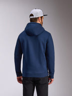 Alpinestars Frontal Hoodie, marinblå fleece-huvtröja, baksida av avslappnad streetwear, bärs med svarta byxor och en vit och svart meshkeps, modern motorsport-inspirerad design