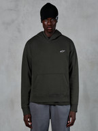 Alpinestars Essentials Ageless Huvtröja, avslappnad streetwear, Off Black pullover med en liten vit Alpinestars-logotyp på bröstet, bärs med en svart mössa, minimalistisk design med känguruficka framtill och plaggstenstvättad finish.
