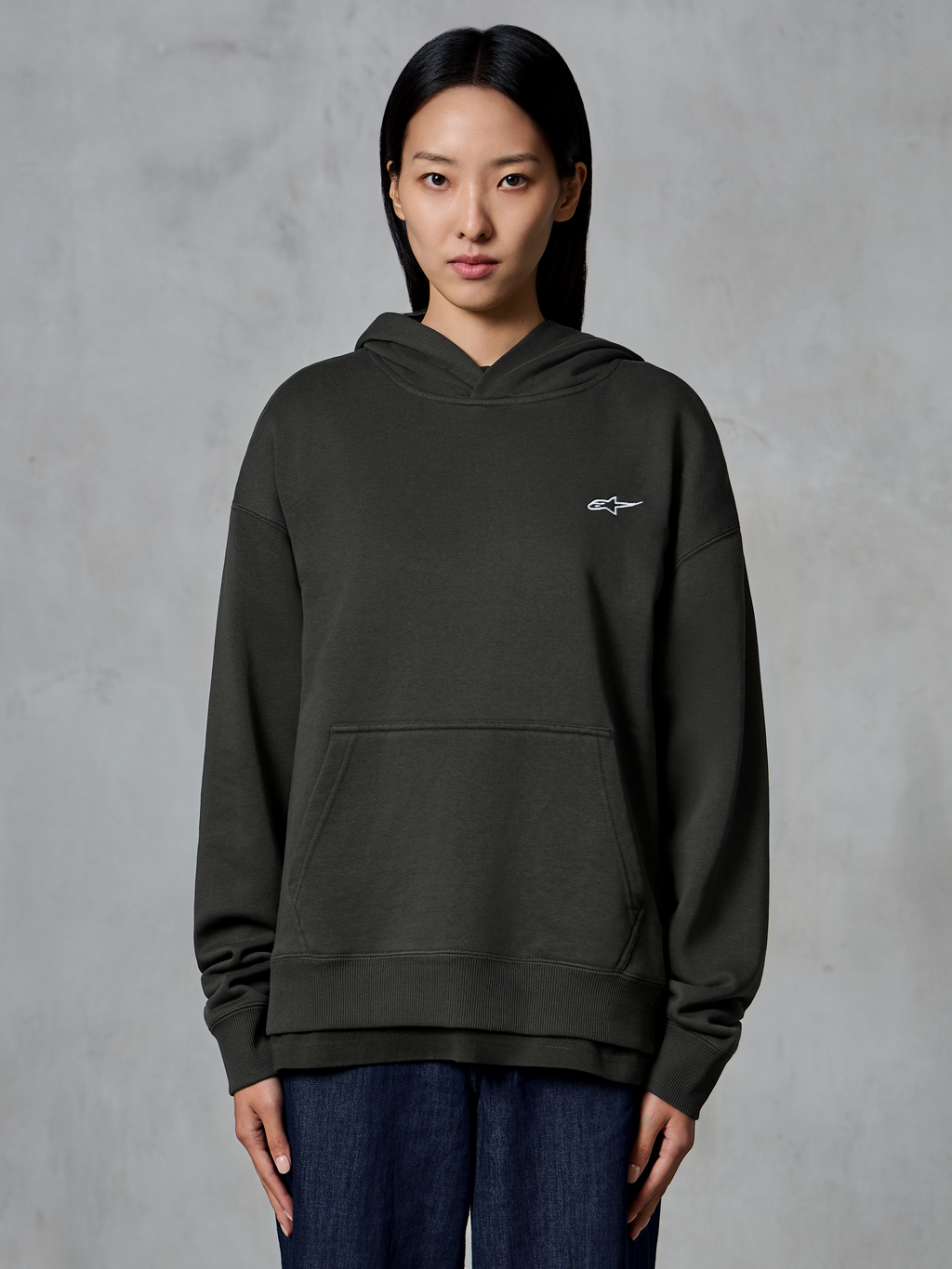 Alpinestars Essentials Ageless Hoodie, Off Black, bärs av en modell, med en liten vit Astars-logotyp på bröstet, känguruficka fram, stentvättad finish, avslappnad premium fleece-streetwear