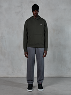 Modell som bär Alpinestars Essentials Ageless Hoodie, casual streetwear, Off Black med liten vit logotyp på bröstet, kombinerad med grå joggers, svart mössa och svarta sneakers, minimalistisk motorsportinspirerad design