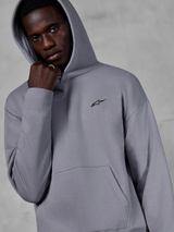 Alpinestars Essentials Ageless Hoodie, Silver, manlig modell som bär huvtröjan med huvan uppfälld, liten svart Alpinestars-logotyp på bröstet, känguruficka, ribbade muddar, avslappnad lifestyle streetwear