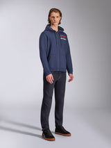 Manlig modell i Alpinestars Formulation Hoodie, marinblå polyfleece med dragkedja fram, röd och vit logotyp på bröstet, matchat med mörka jeans och svarta sneakers, avslappnad motorsportinspirerad streetwear