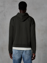 Alpinestars Essentials Ageless Zip Hoodie, vy bakifrån av en huvtröja med avslappnad passform i Off Black, bärs med en vit t-shirt och blå jeans, stilren och diskret motorsportinspirerad sportklädsel.