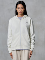 Alpinestars Essentials Ageless Zip Hoodie, Off White, huvtröja i fleece med dragkedja som bärs av en modell, med en liten svart Astars-logotyp på bröstet, avslappnad passform, vardagligt motorsportinspirerat livsstilsplagg