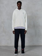 Alpinestars Essentials Ageless Zip Hoodie, benvit huvtröja med dragkedja, avslappnad passform med en liten svart logotyp på bröstet, bärs med svarta mjukisbyxor och sneakers, avslappnat motorsportinspirerat streetwear.