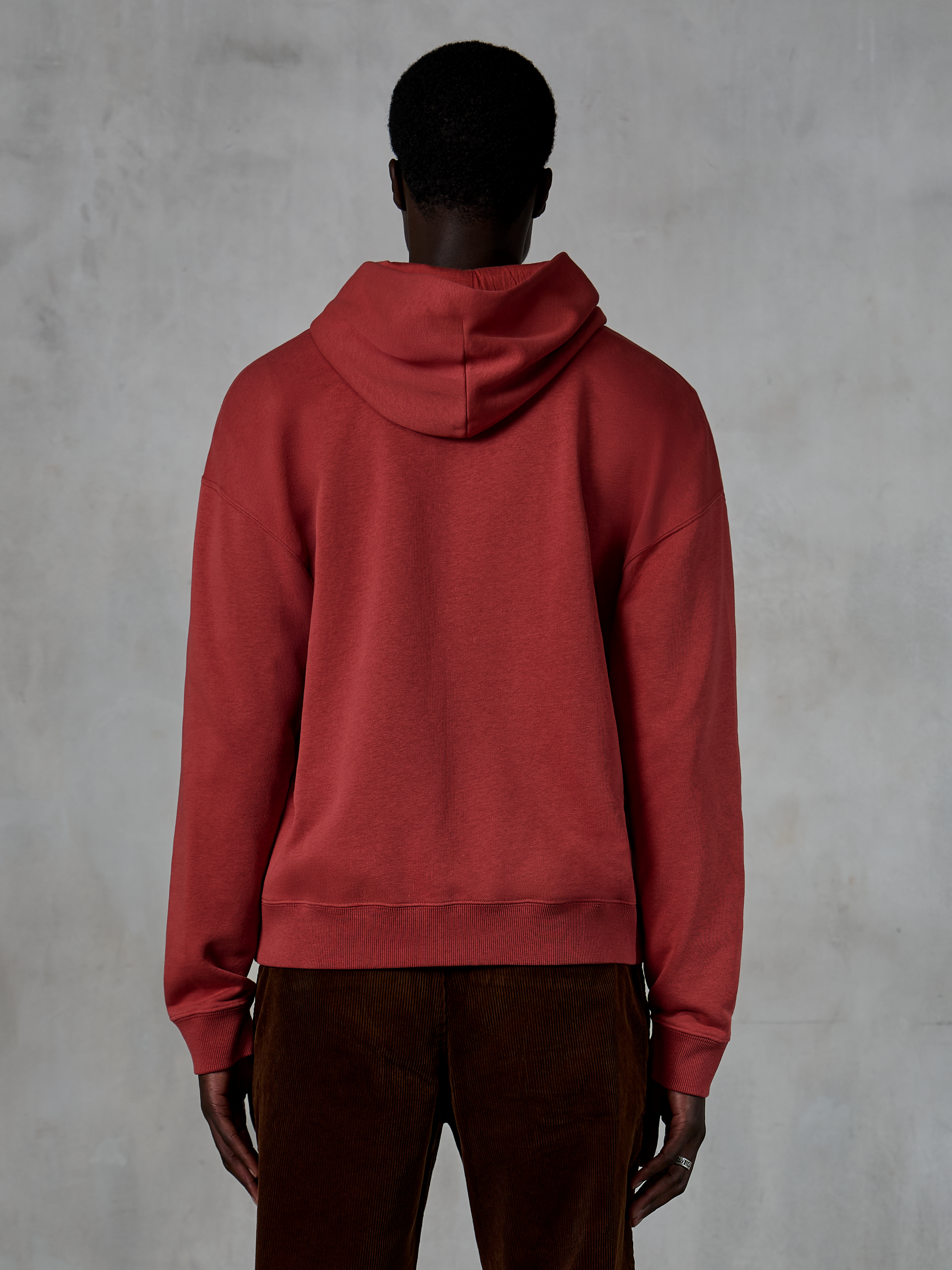 Alpinestars Essentials Ageless Zip Hoodie, tegelröd, vy bakifrån som visar avslappnad passform och huva med dragsko, bärs med bruna manchesterbyxor, avslappnad motorsport-inspirerad streetwear