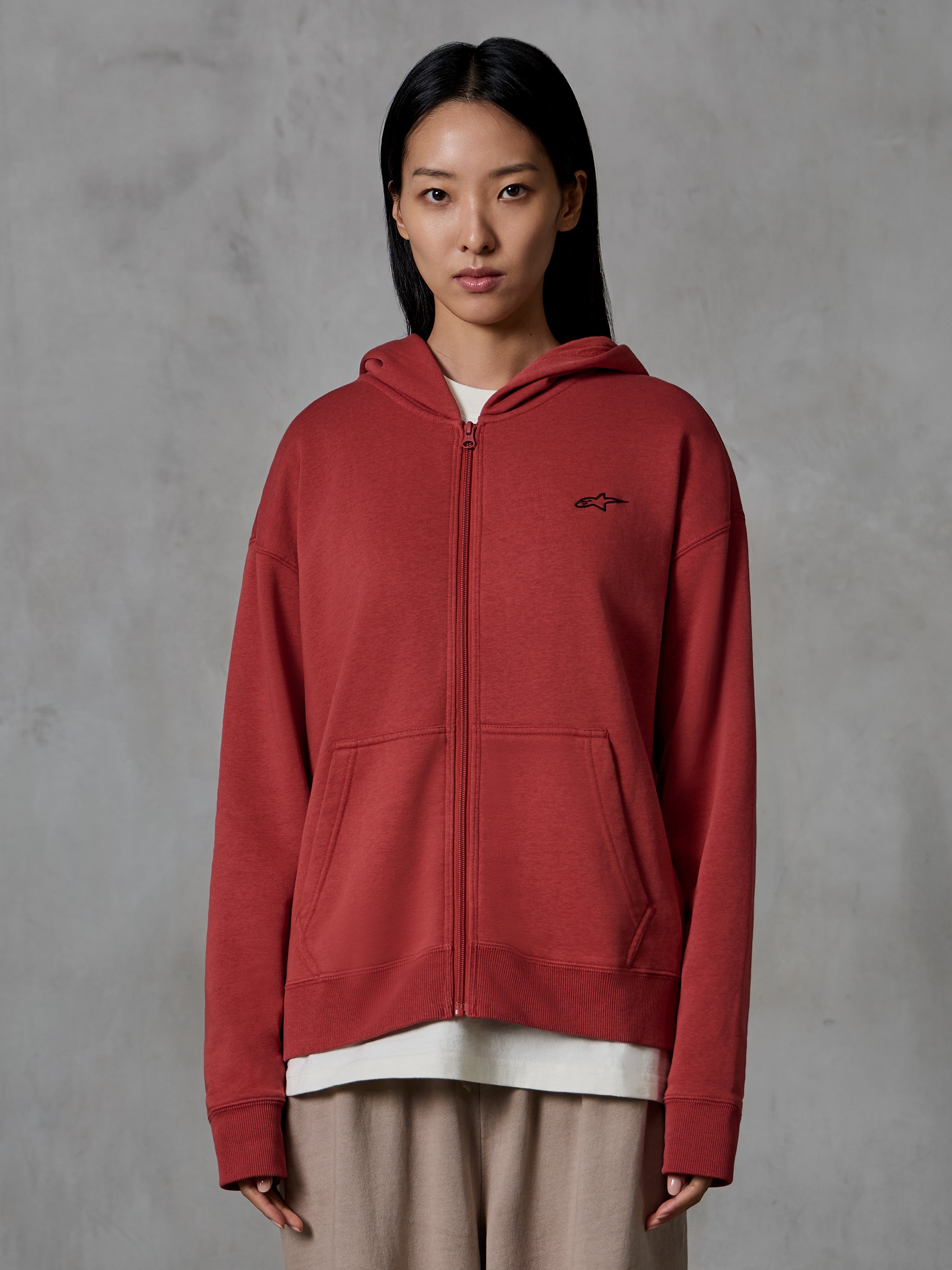 Alpinestars Essentials Ageless Zip Hoodie, tegelröd, avslappnad streetwear, bärs av en modell, design med hel dragkedja och huva, liten svart Alpinestars-logotyp på bröstet, avslappnad passform i kompakt fleece.