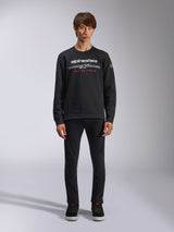 Alpinestars Bettern Crew, Black Crew Neck Sweatshirt, features white alpinestars logo with grey horizontal stripes and red 'RACING AHEAD' text, casual motorsport streetwear, worn by model with black pants and sneakers