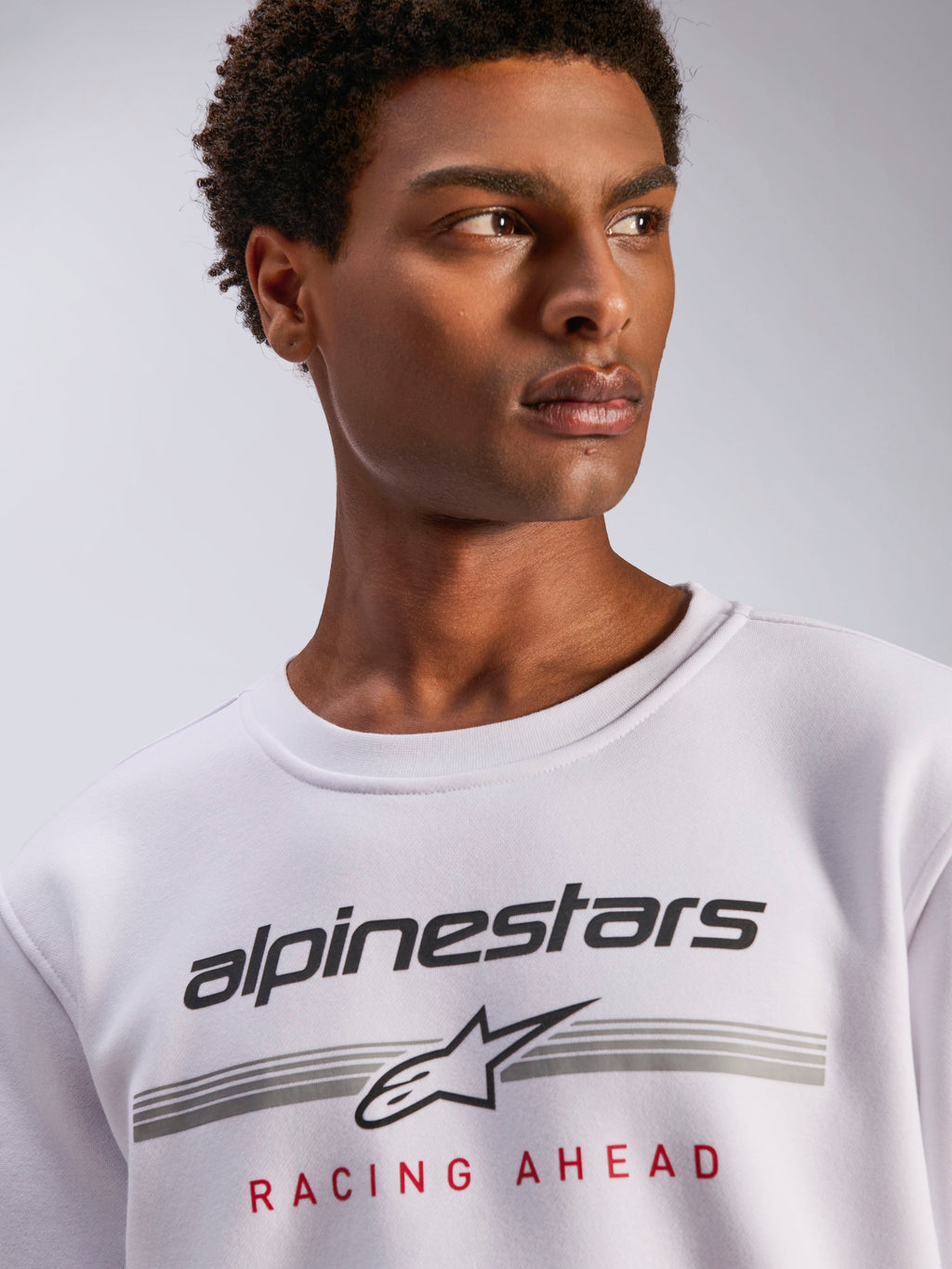 Alpinestars Bettern Crew, vit sweatshirt i fleece med rund hals, svart Alpinestars-logotyp med grå horisontella linjer och röd 'Racing Ahead'-text, avslappnad motorsportinspirerad streetwear