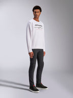 Alpinestars Bettern Crew, vit sweatshirt, med svart Alpinestars-logotyp och röd 'Racing Ahead'-text, casual motorsport-streetwear, buren av en modell med mörka byxor och svarta sneakers