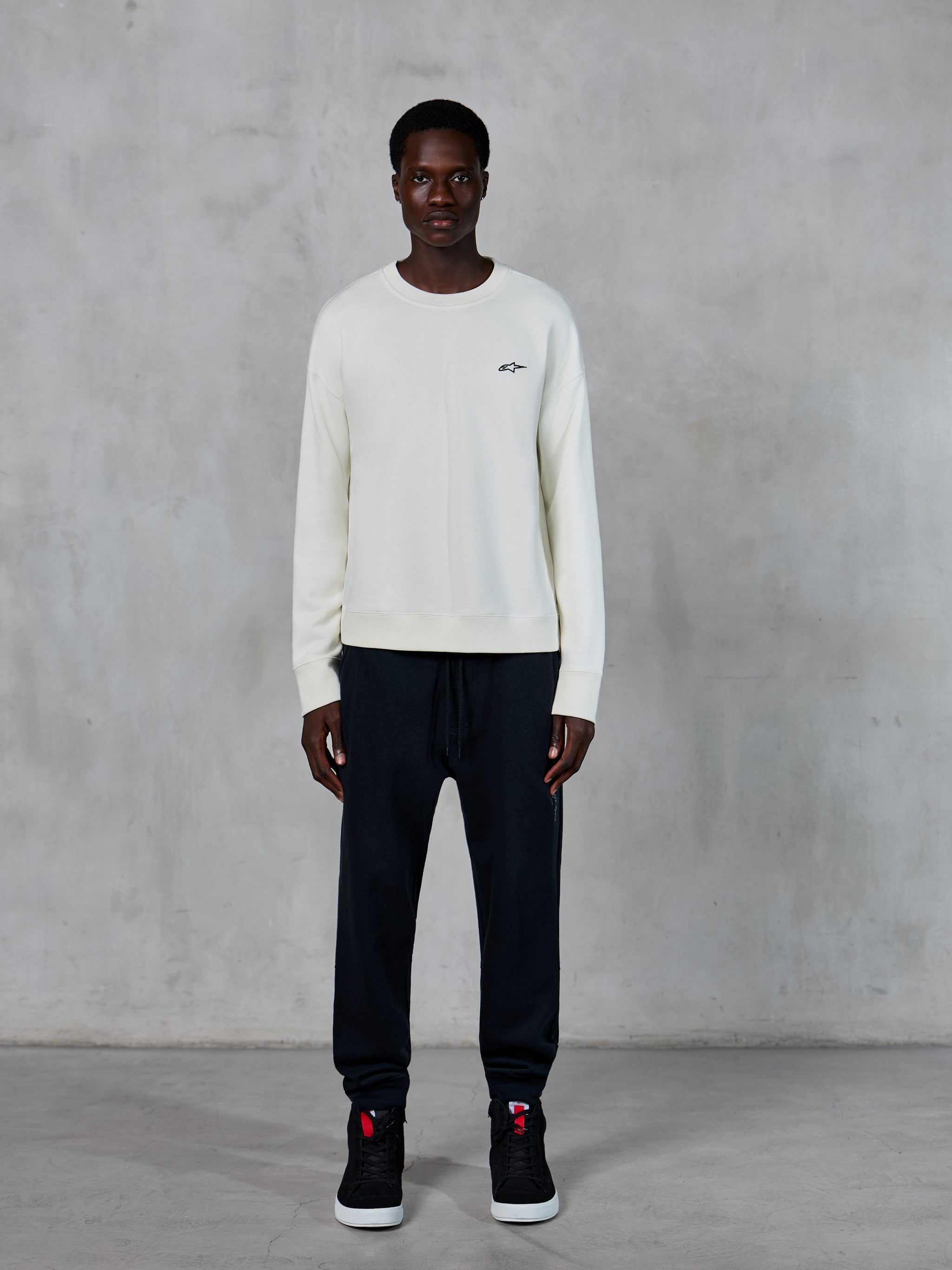 Alpinestars Essentials Ageless Crew, crewneck-sweatshirt, off-white med liten svart stjärnlogotyp, bärs av modell med svarta joggers, avslappnad motorsport-inspirerad streetwear