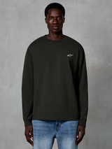 Alpinestars Essentials Ageless LS Tee, långärmad t-shirt, Off Black, med en liten vit Alpinestars-logotyp på bröstet, bärs av en modell med blå jeans, vardaglig streetwear i ekologisk bomull