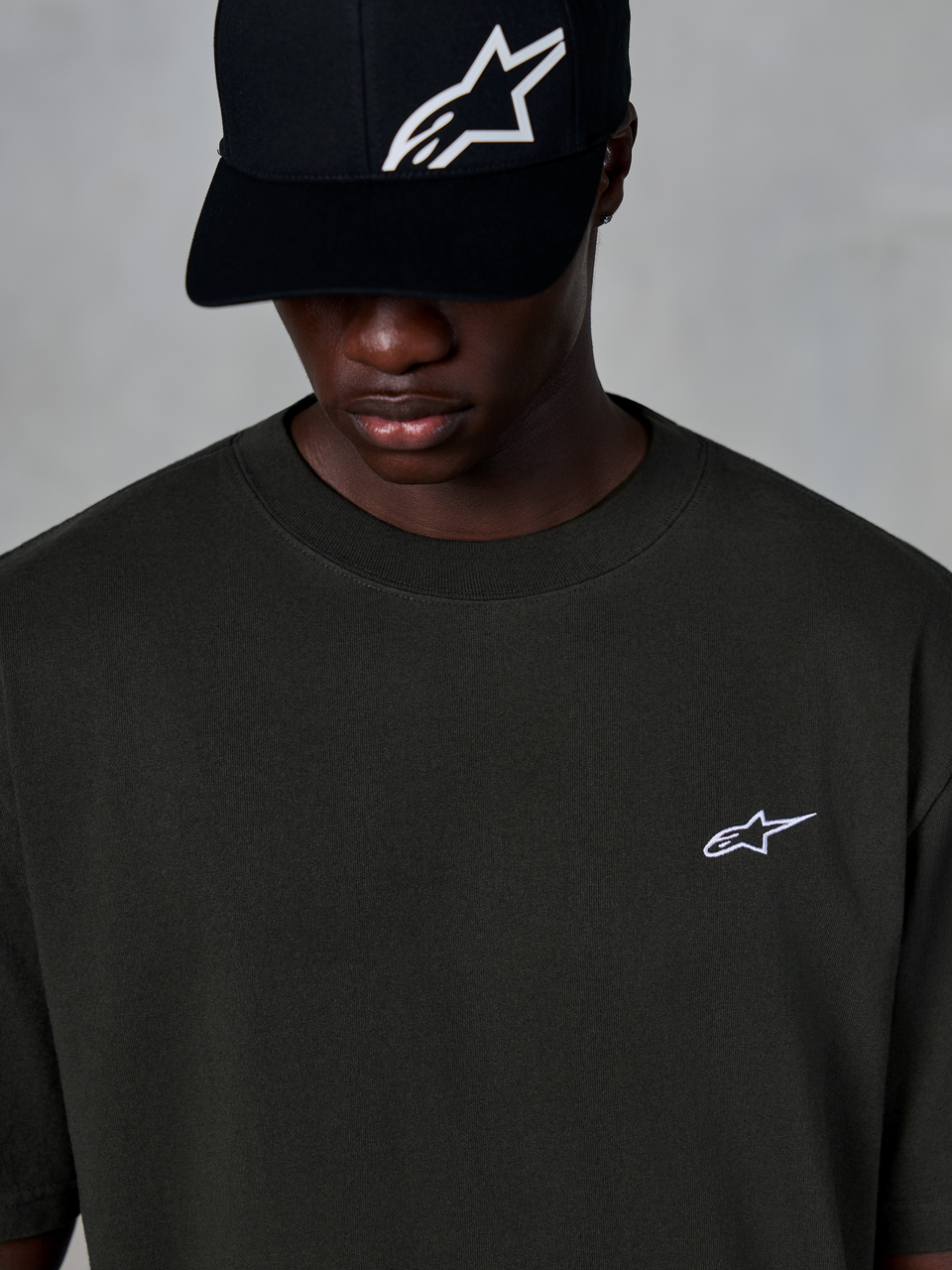 Alpinestars Essentials Ageless SS Tee, kortärmad t-shirt, off black, med en liten vit Alpinestars-logotyp på bröstet, bärs med en svart baseballkeps med logotyp, avslappnad motorsport-streetwearstil