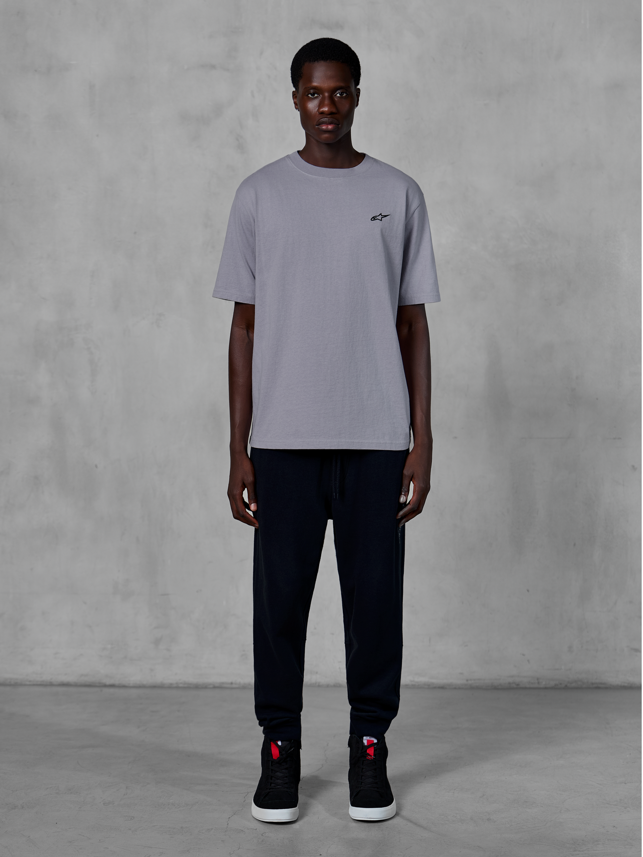 Alpinestars Essentials Ageless SS Tee, kortärmad t-shirt, silver, med en liten svart logotyp på bröstet, stylad med svarta joggers och sneakers, avslappnad motorsport-streetwear