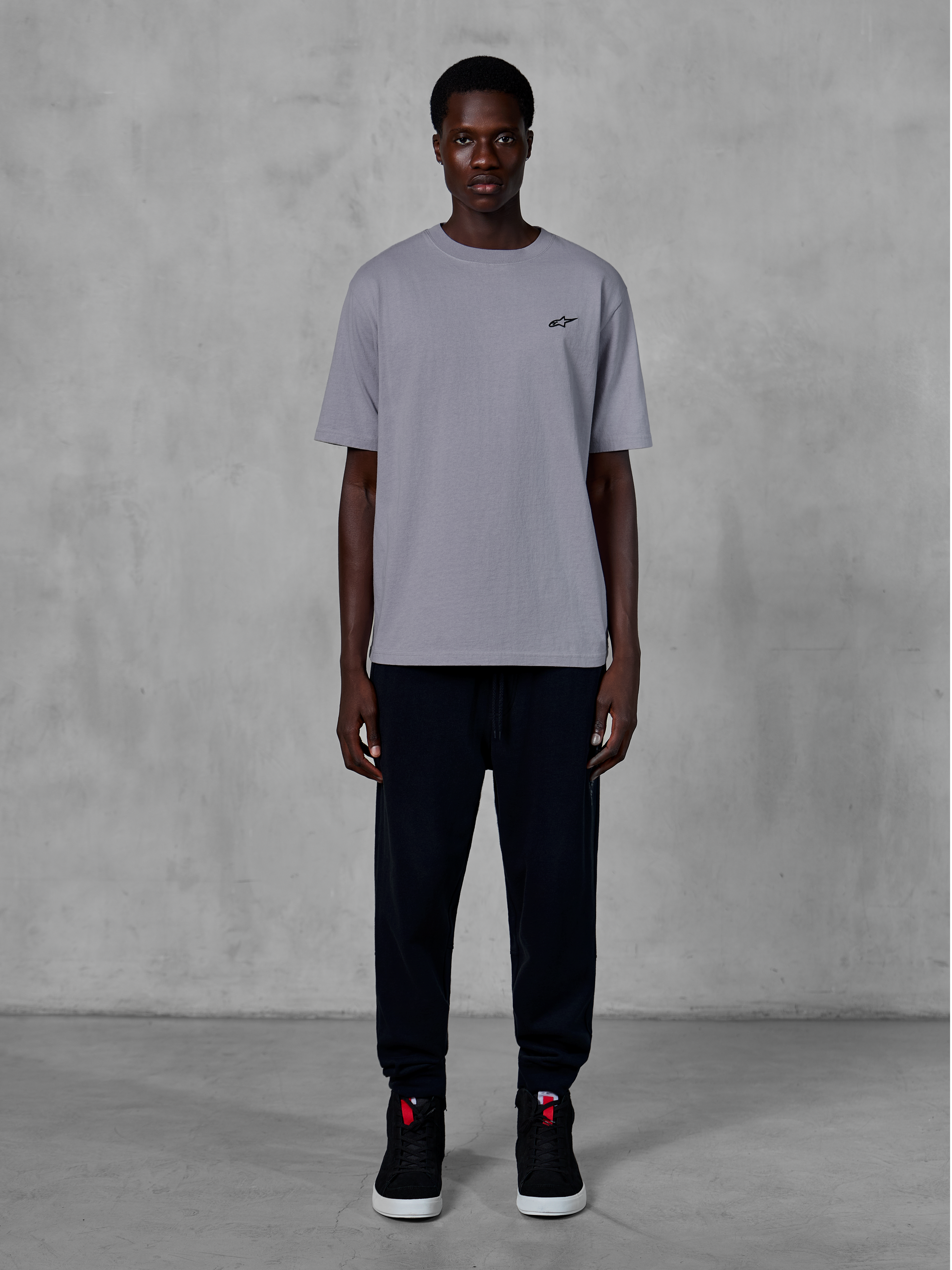 Alpinestars Essentials Ageless SS Tee, kortärmad t-shirt, silver, med en liten svart logotyp på bröstet, stylad med svarta joggers och sneakers, avslappnad motorsport-streetwear