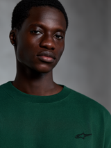 Alpinestars Essentials Ageless SS Tee, Pine Green kortärmad t-shirt, närbild på modell som bär grön t-shirt i ekologisk bomull med liten broderad logotyp, avslappnad streetwear-design