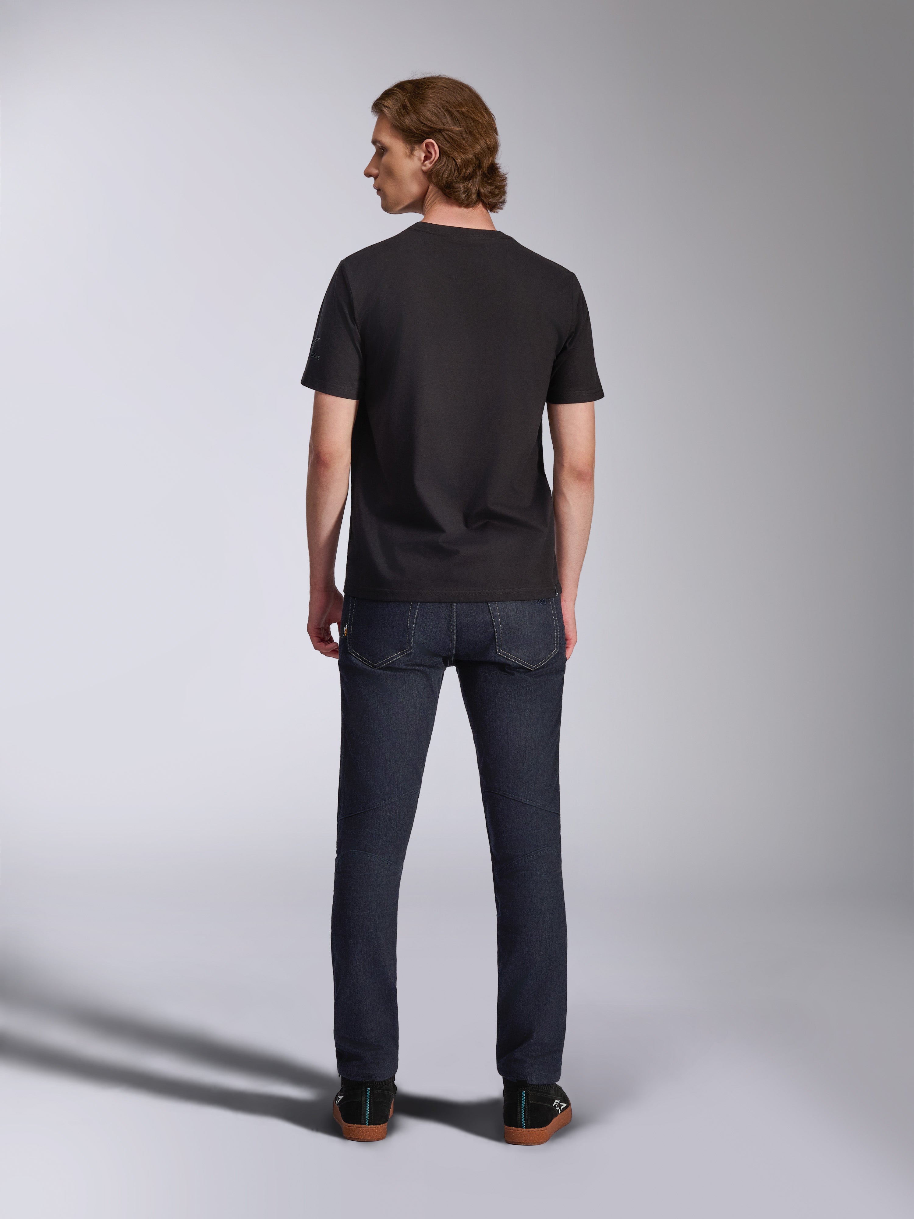 Alpinestars Global CSF T-shirt, kortärmad tröja i svart, ryggvy av manlig modell som bär t-shirten med mörka jeans, avslappnat motorsportinspirerat streetwear