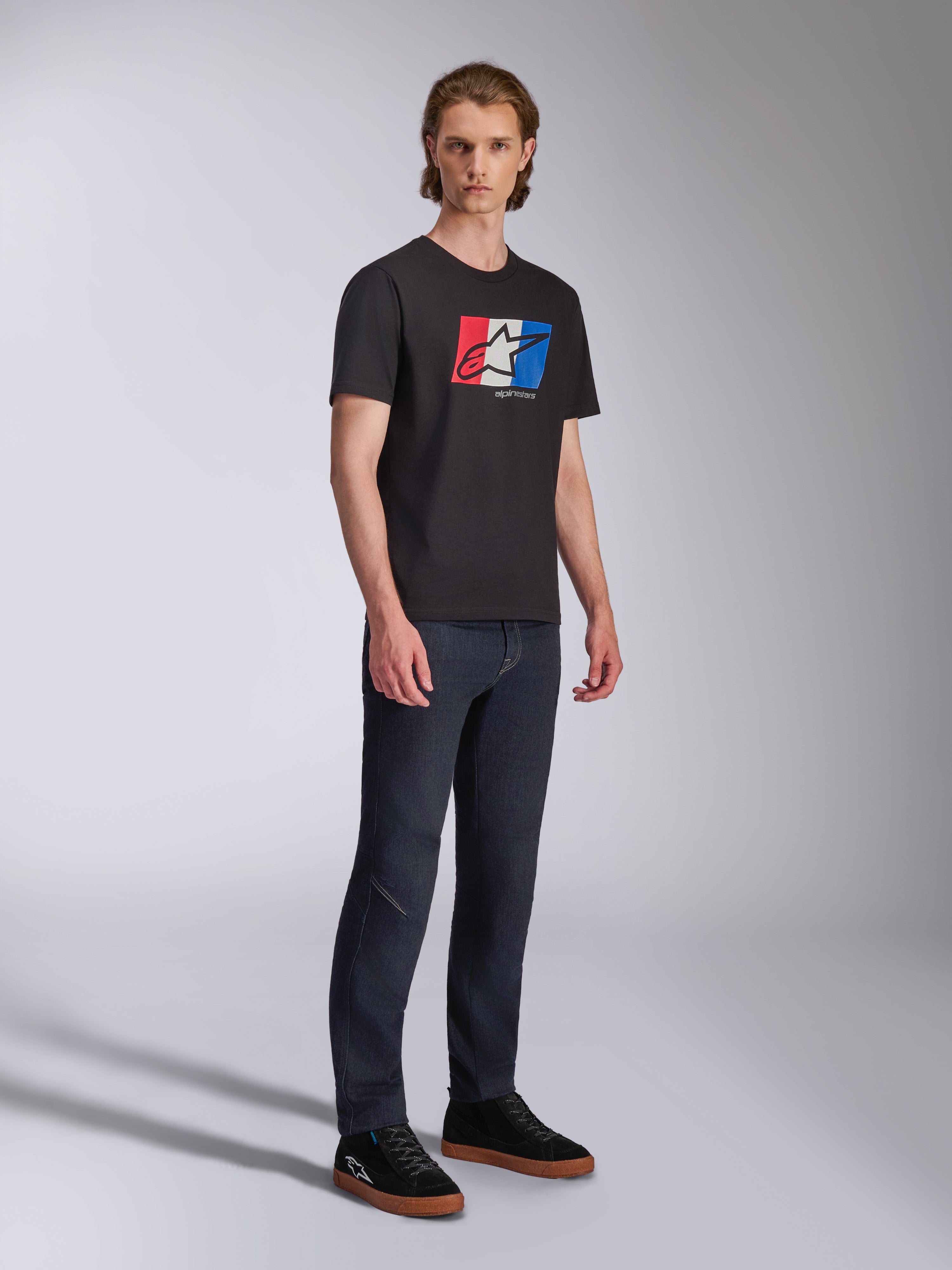 Alpinestars Global CSF T-shirt, kortärmad t-shirt, svart med röd, vit och blå logotypgrafik, casual motorsport-streetwear, helkroppsbild av modell i mörka jeans och svarta sneakers