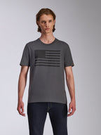 Alpinestars Waving CSF Tee, kortärmad t-shirt, mörkgrå, med en svart flagginspirerad Blaze-logografik på bröstet, bärs av en modell med mörka jeans, avslappnat motorsport-streetwear