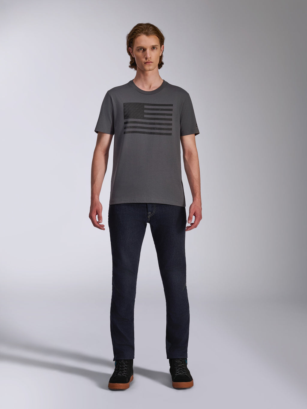 Alpinestars Waving CSF Tee, kortärmad t-shirt, koksgrå, svart Blaze 2.0-logografik i flaggstil, avslappnad motorsport-streetwear, bärs med mörka denimjeans