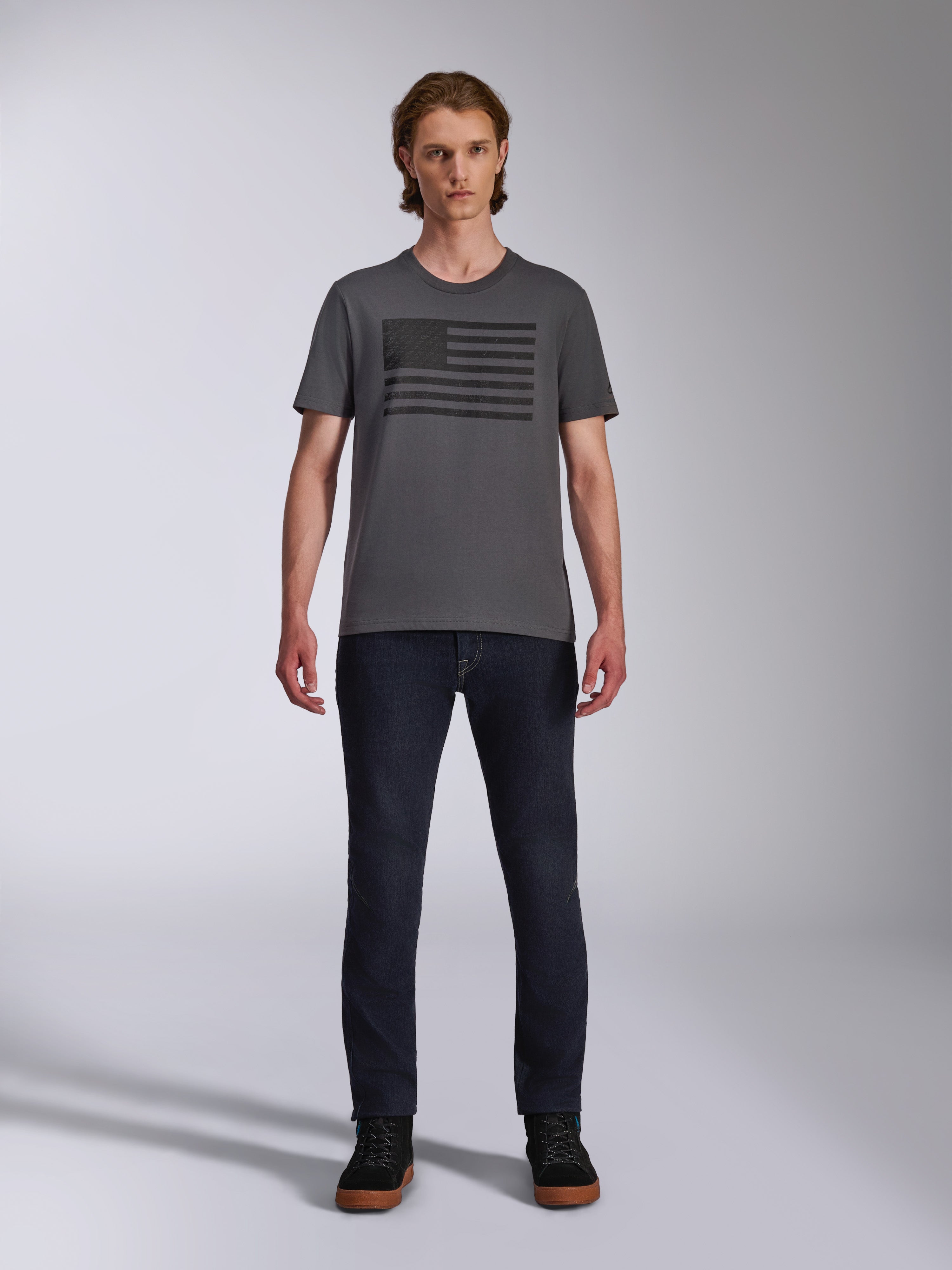 Alpinestars Waving CSF Tee, kortärmad t-shirt, koksgrå, svart Blaze 2.0-logografik i flaggstil, avslappnad motorsport-streetwear, bärs med mörka denimjeans