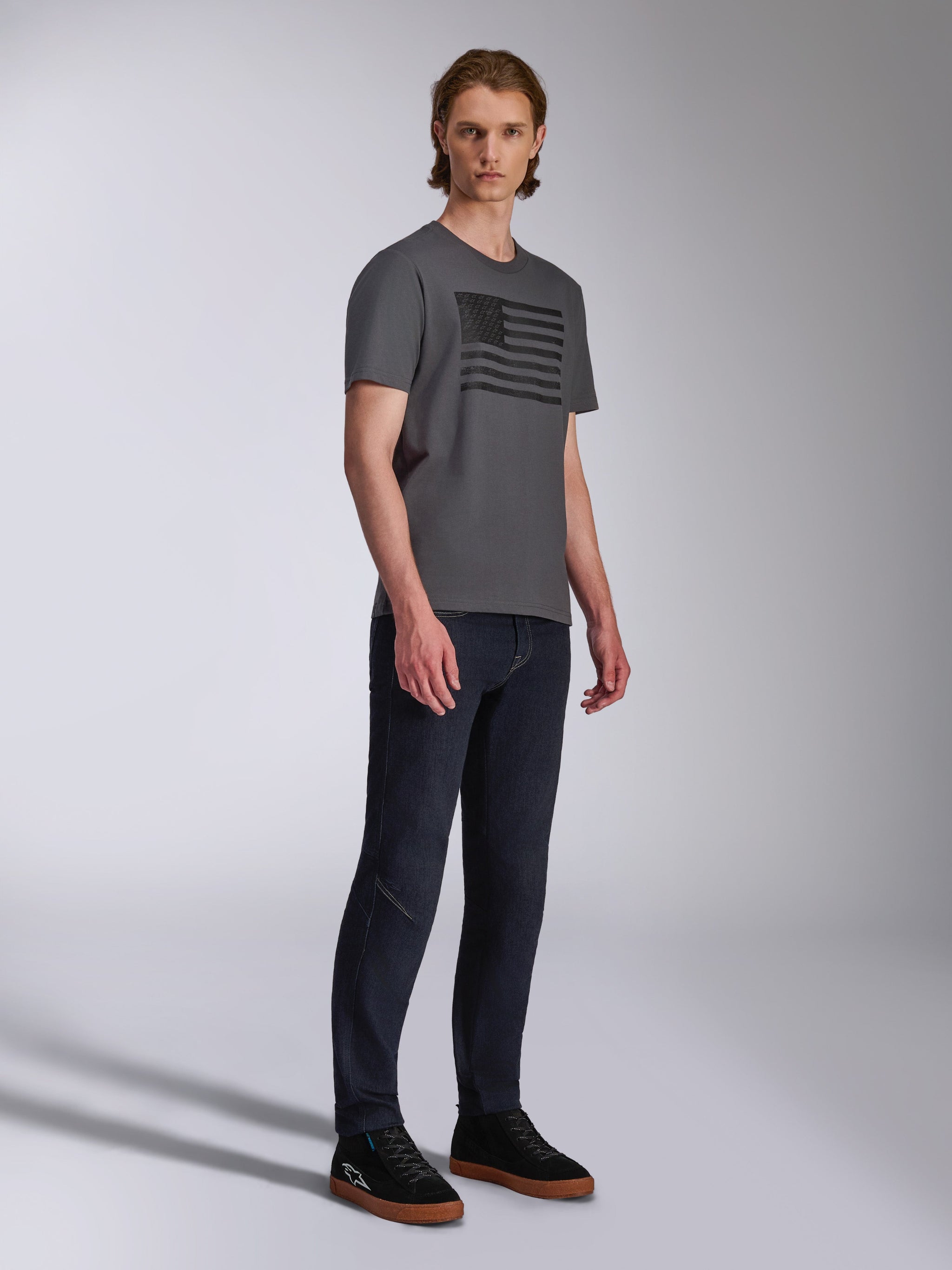 Alpinestars Waving CSF Tee, Short Sleeve T-Shirt, Charcoal, Black Waving Flag Graphic, worn by a model with dark jeans and sneakers, Casual Motorsport Streetwear