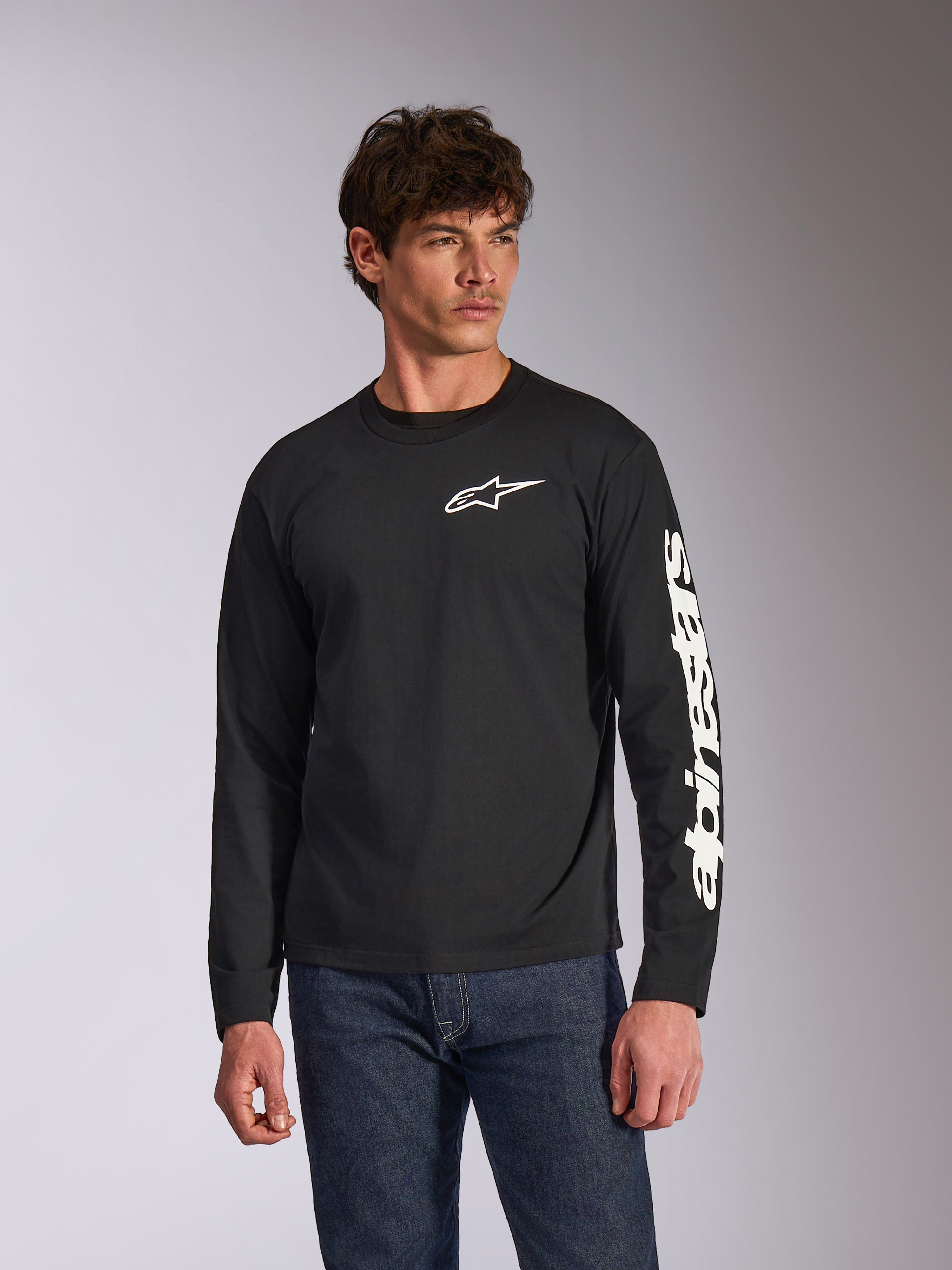 Alpinestars Trackside CSF långärmad t-shirt, svart, vit Alpinestars-logotyp på bröstet och märkning på ärmen, bärs av en modell med blå jeans, avslappnad motorsport-streetwear